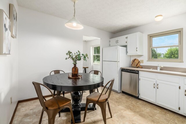 kitchen with stainless steel dishwasher, freestanding refrigerator, a sink, white cabinetry, and a textured ceiling