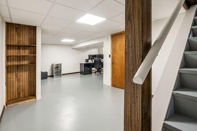 finished below grade area with a paneled ceiling, an office area, and stairway