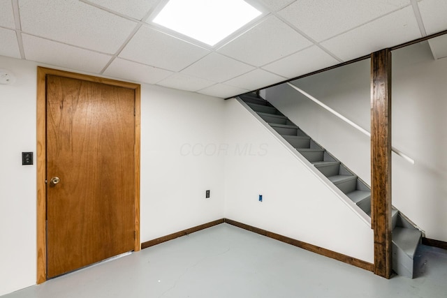 finished below grade area featuring a drop ceiling, stairs, and baseboards