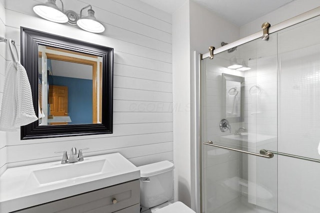 full bath with wooden walls, toilet, a shower stall, and vanity