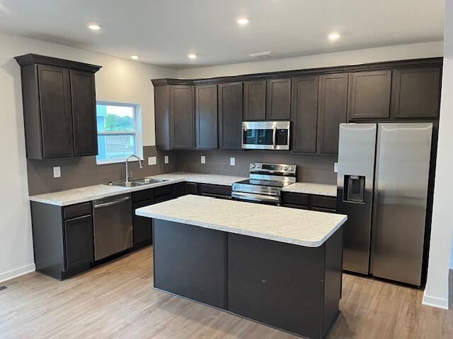 kitchen with a sink, appliances with stainless steel finishes, light wood-style floors, light countertops, and a kitchen island