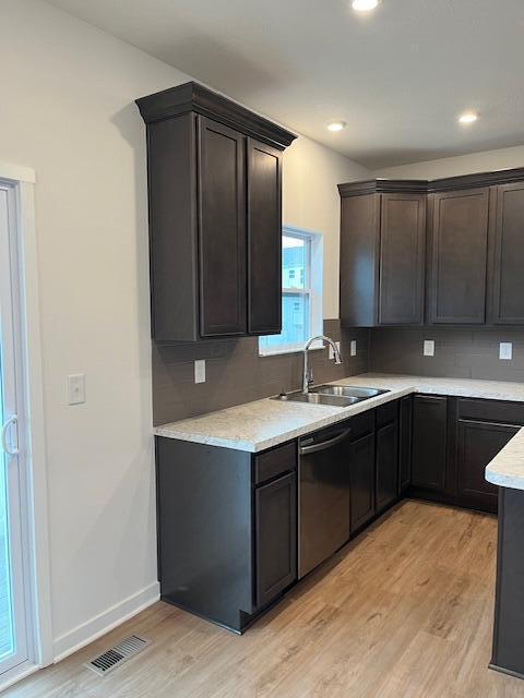kitchen featuring light wood-style flooring, a sink, visible vents, dishwasher, and backsplash