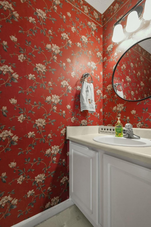 bathroom featuring baseboards, wallpapered walls, and vanity