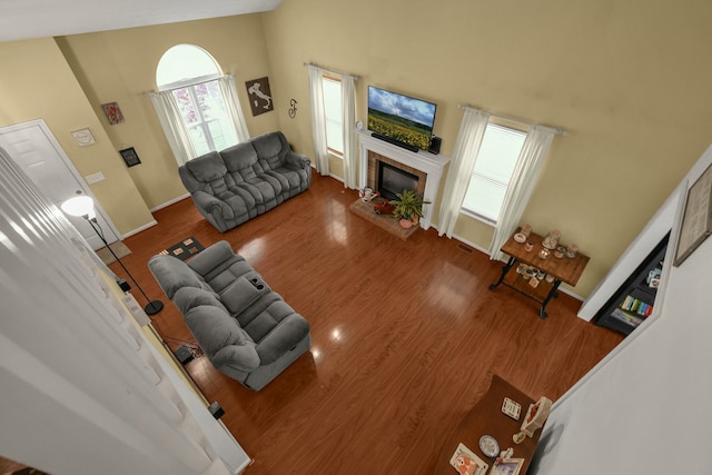 living area with visible vents, a fireplace, wood finished floors, high vaulted ceiling, and baseboards