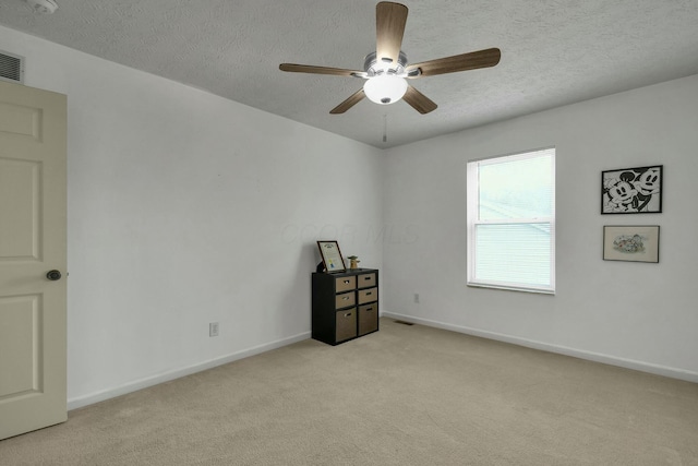 spare room with baseboards, a ceiling fan, a textured ceiling, and light colored carpet