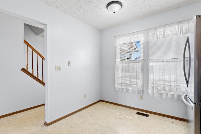 empty room with a textured ceiling, visible vents, baseboards, and stairway