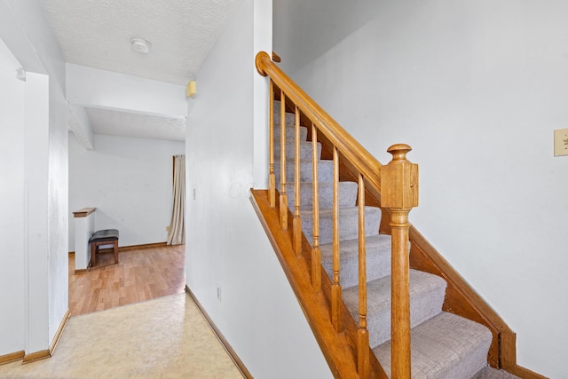 staircase featuring a textured ceiling, baseboards, and wood finished floors