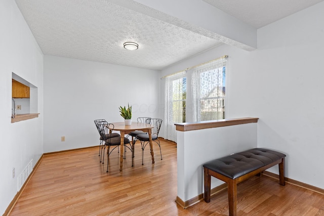dining area featuring a textured ceiling, baseboards, visible vents, and light wood finished floors