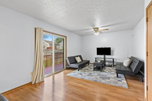 living room featuring light wood-type flooring, a ceiling fan, a textured ceiling, and baseboards