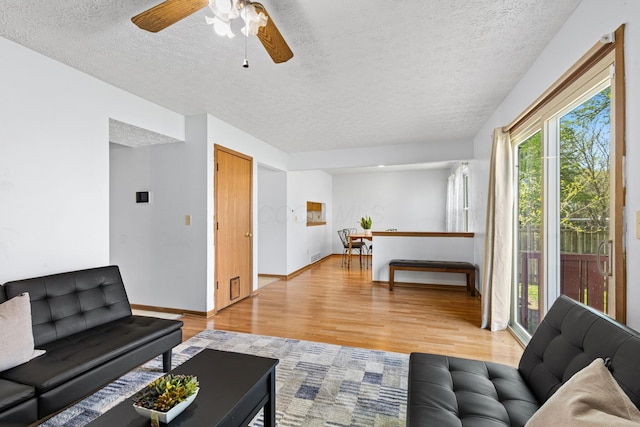 living room with light wood-type flooring, a ceiling fan, a textured ceiling, and a wealth of natural light