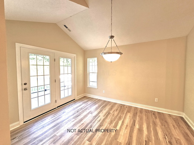 unfurnished dining area with visible vents, wood finished floors, baseboards, a textured ceiling, and vaulted ceiling