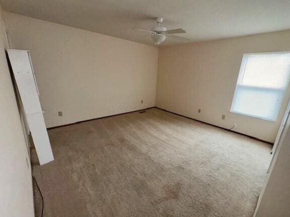 carpeted empty room featuring a ceiling fan and baseboards