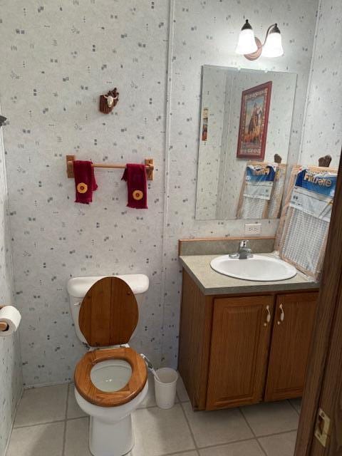 half bath with toilet, vanity, wallpapered walls, and tile patterned floors