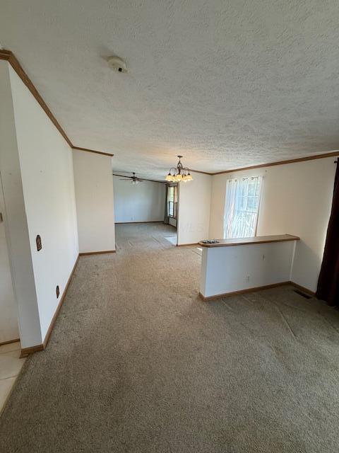 empty room featuring ornamental molding, an inviting chandelier, a textured ceiling, and light colored carpet