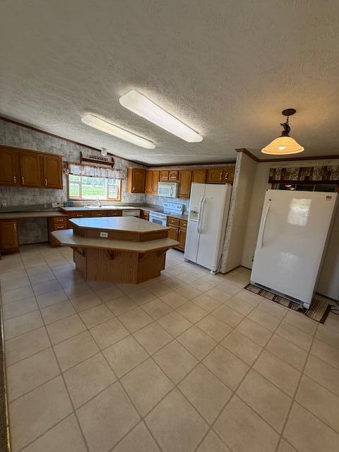 kitchen with brown cabinets, light tile patterned flooring, a center island, white appliances, and a textured ceiling