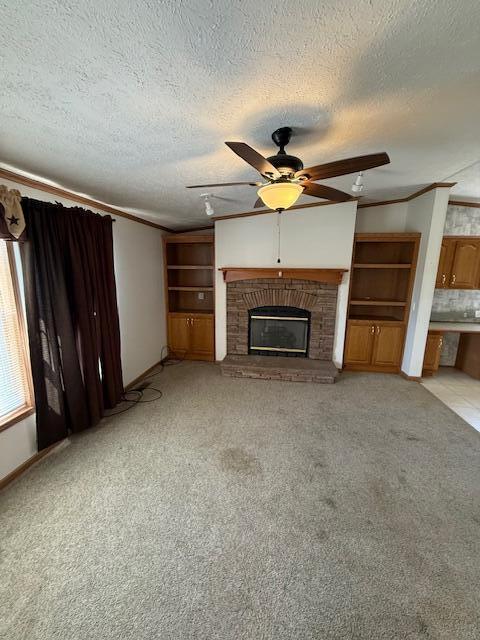 unfurnished living room with a brick fireplace, a ceiling fan, ornamental molding, a textured ceiling, and light colored carpet