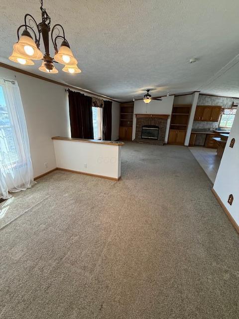 unfurnished living room with ceiling fan with notable chandelier, light carpet, a glass covered fireplace, baseboards, and a textured ceiling