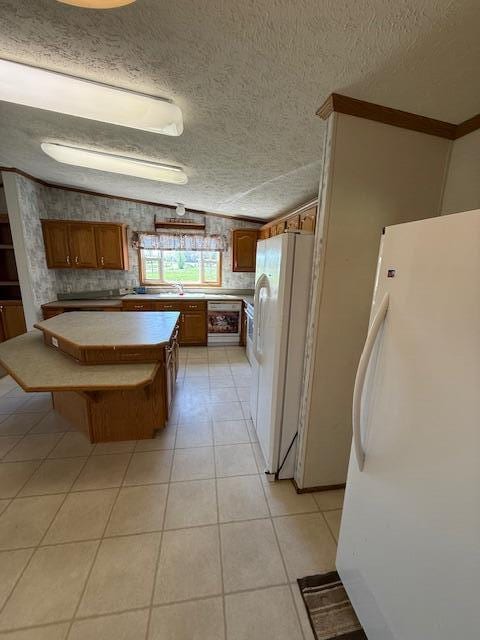 kitchen with a textured ceiling, brown cabinets, and freestanding refrigerator