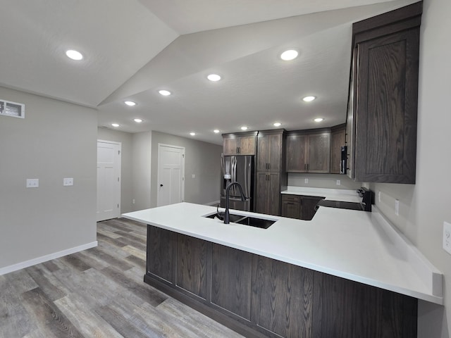 kitchen with dark brown cabinets, range with electric cooktop, light countertops, a sink, and vaulted ceiling