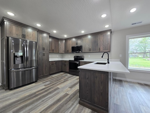 kitchen featuring a sink, light wood finished floors, stainless steel appliances, a peninsula, and visible vents