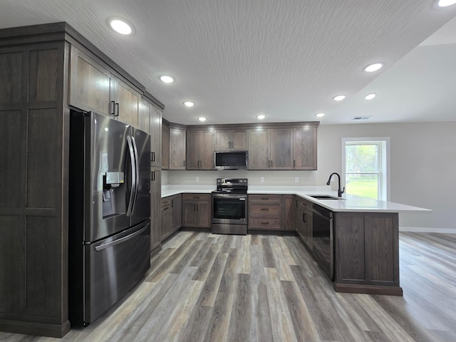 kitchen featuring appliances with stainless steel finishes, a sink, light countertops, a peninsula, and light wood-type flooring