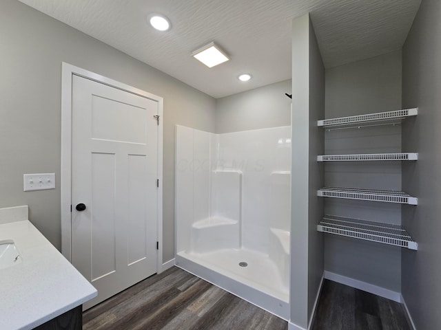 bathroom with vanity, baseboards, walk in shower, and wood finished floors