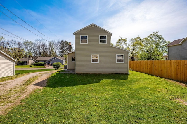 rear view of property featuring fence, driveway, and a lawn