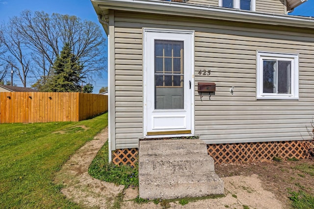doorway to property with fence and a lawn