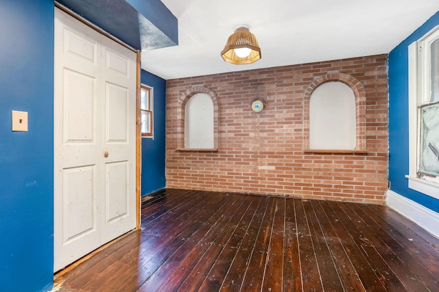 unfurnished room featuring hardwood / wood-style floors and brick wall