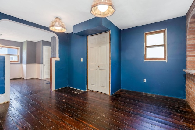empty room featuring arched walkways, a wainscoted wall, and wood-type flooring