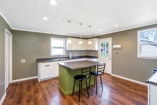 kitchen with a sink, ornamental molding, dark countertops, dishwasher, and white cabinets