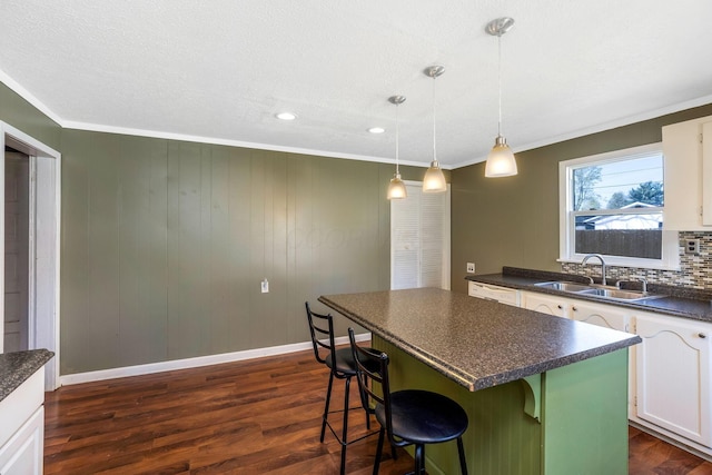 kitchen with a sink, a kitchen bar, white dishwasher, dark countertops, and white cabinets