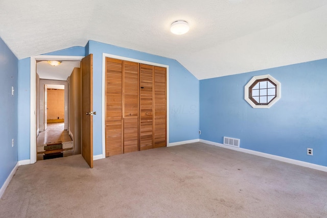 unfurnished bedroom with visible vents, baseboards, a closet, vaulted ceiling, and carpet