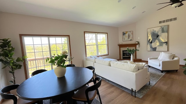 living area featuring visible vents, a glass covered fireplace, wood finished floors, and vaulted ceiling