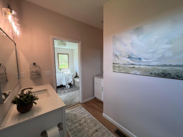 ensuite bathroom with visible vents, wood finished floors, vanity, baseboards, and ensuite bathroom