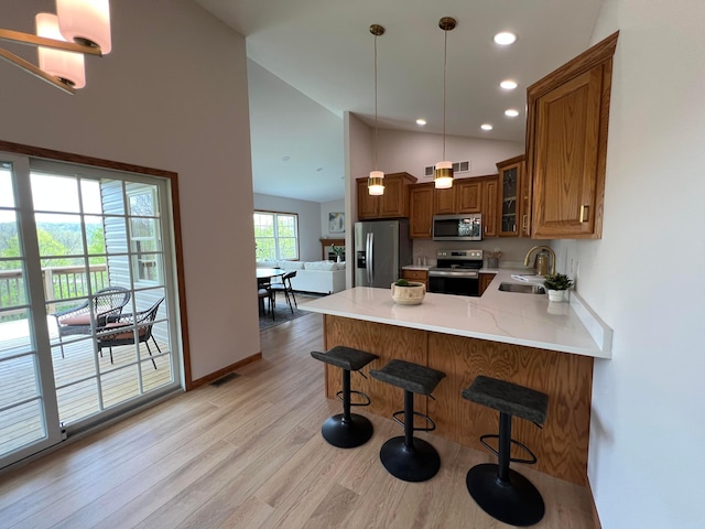 kitchen featuring brown cabinetry, a peninsula, glass insert cabinets, a sink, and appliances with stainless steel finishes