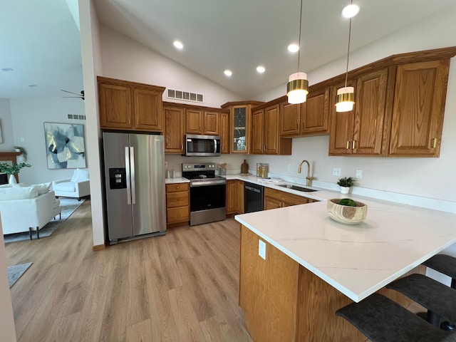 kitchen featuring appliances with stainless steel finishes, a sink, brown cabinetry, a peninsula, and visible vents