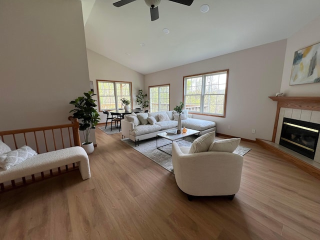 living area with a fireplace, light wood-style floors, baseboards, high vaulted ceiling, and a ceiling fan