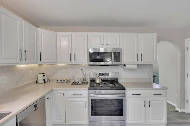 kitchen with white cabinetry, arched walkways, appliances with stainless steel finishes, and light countertops