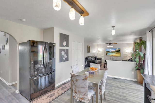 dining space with arched walkways, ceiling fan, light wood-style flooring, and baseboards