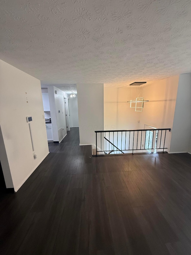interior space with dark wood finished floors, baseboards, a textured ceiling, and an upstairs landing