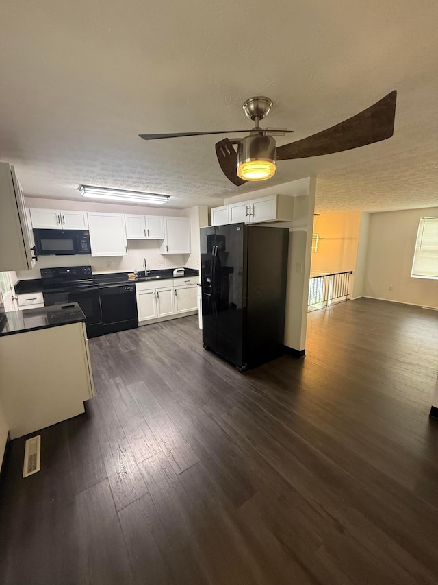 kitchen featuring dark wood-style floors, a sink, black appliances, dark countertops, and white cabinets