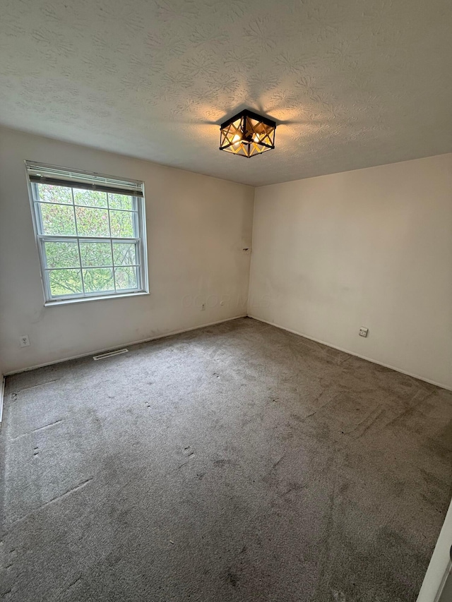 carpeted spare room with visible vents and a textured ceiling