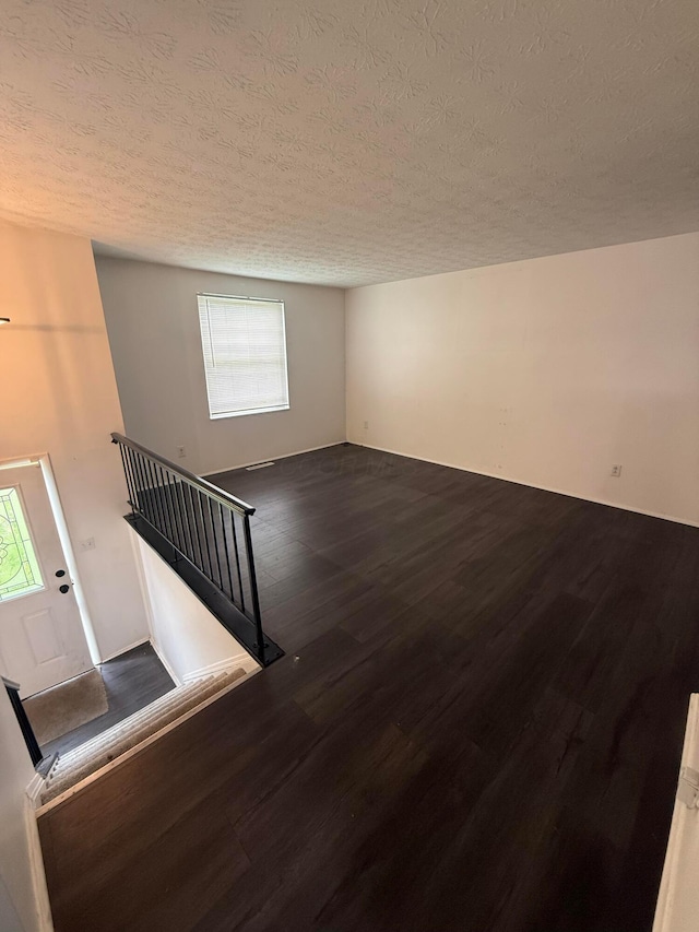 unfurnished living room with a textured ceiling, wood finished floors, and stairway