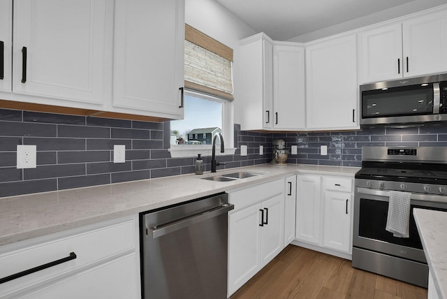kitchen featuring light wood-style floors, white cabinetry, light stone counters, a sink, and stainless steel appliances