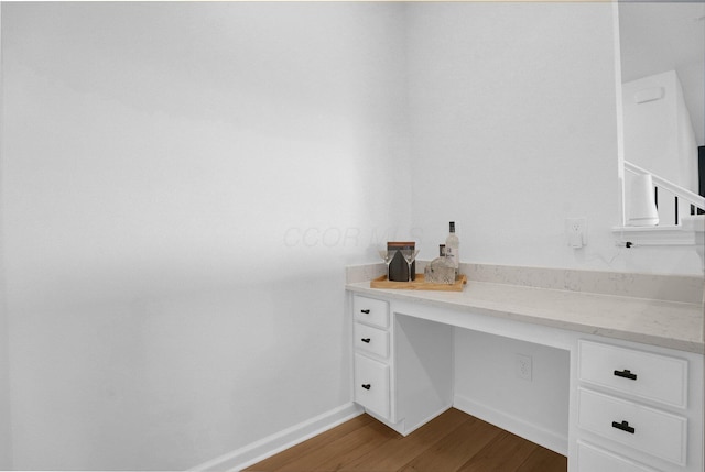 unfurnished office with dark wood-style flooring, baseboards, and built in desk
