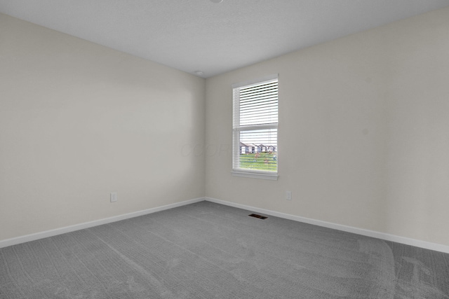 empty room featuring baseboards, visible vents, and dark carpet