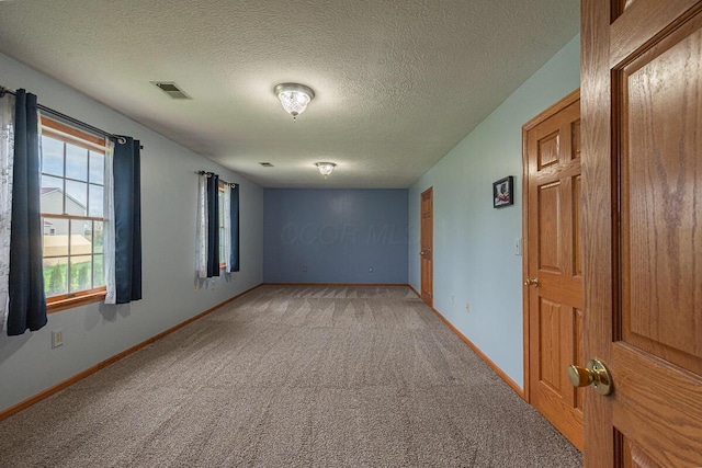 spare room with a textured ceiling, visible vents, baseboards, and light carpet