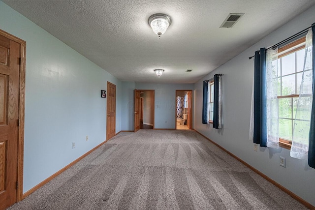 unfurnished room with light colored carpet, a textured ceiling, a wealth of natural light, and visible vents