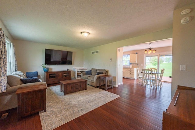 living room featuring a chandelier, a textured ceiling, visible vents, and dark wood-type flooring